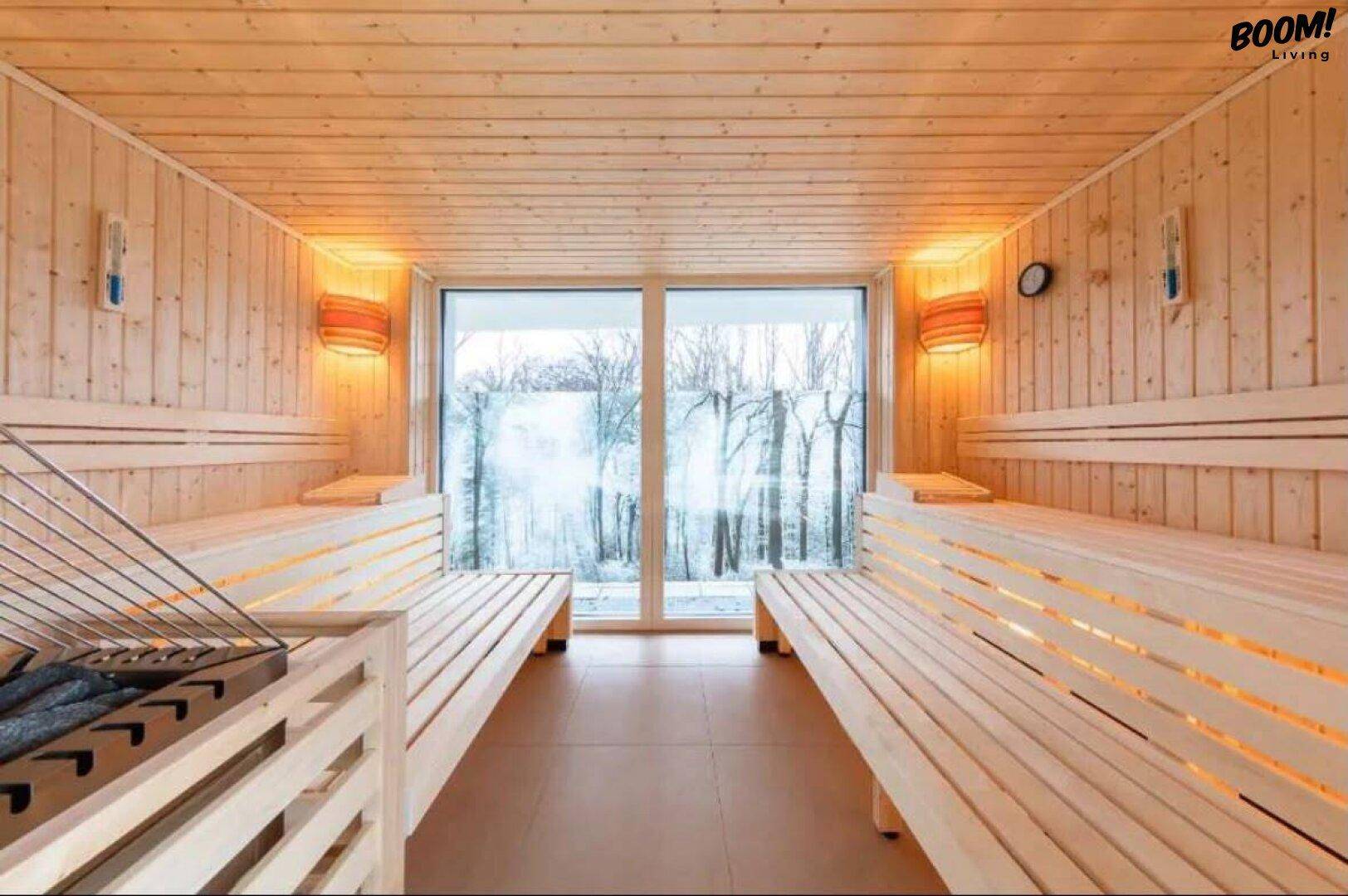 Helle Sauna mit Holzverkleidung und großem Fenster mit Blick auf verschneite Bäume.