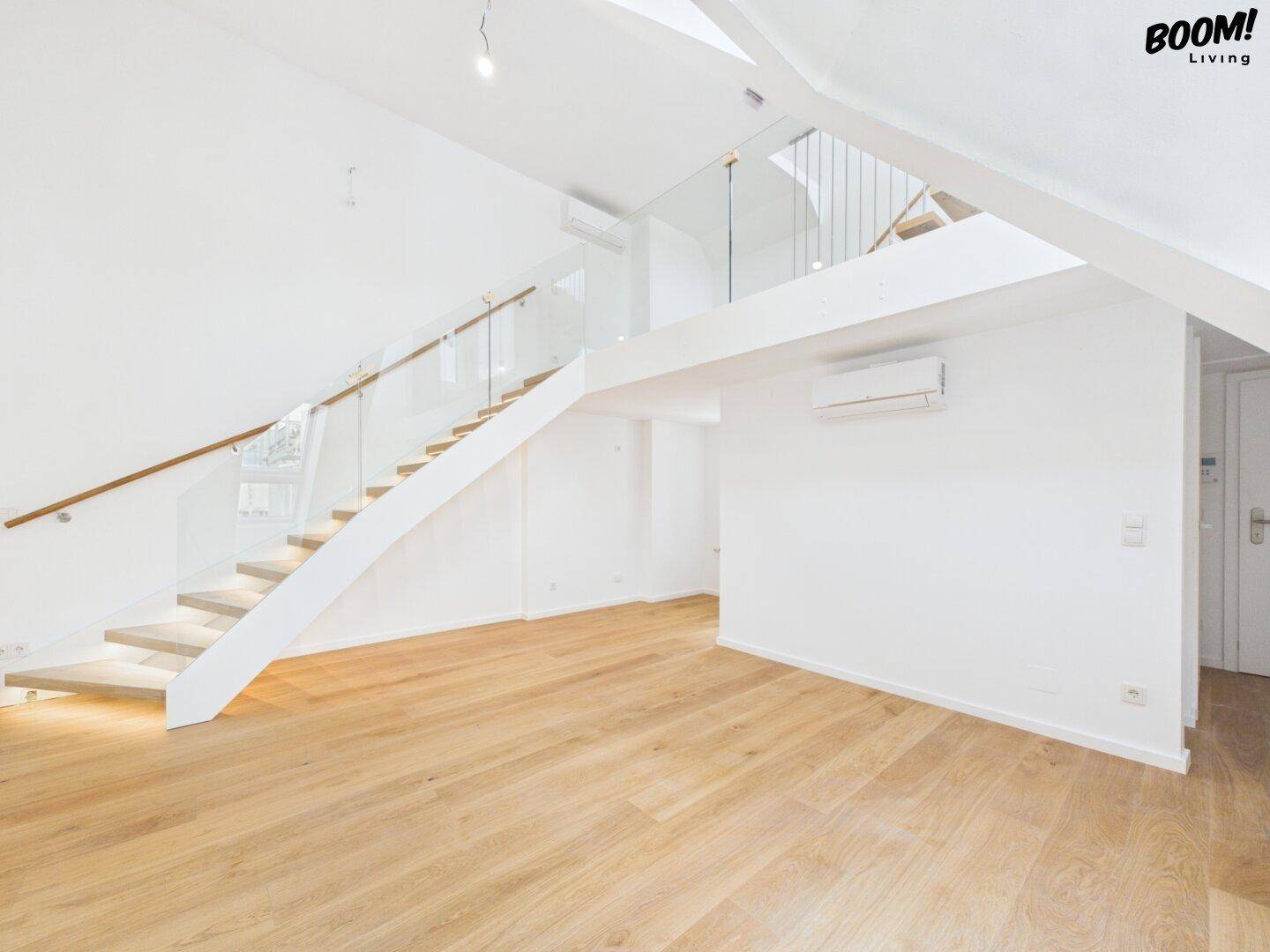 Heller Wohnbereich mit Holzparkett, offener Treppe und Dachschrägen, ausgestattet mit Klimaanlage.