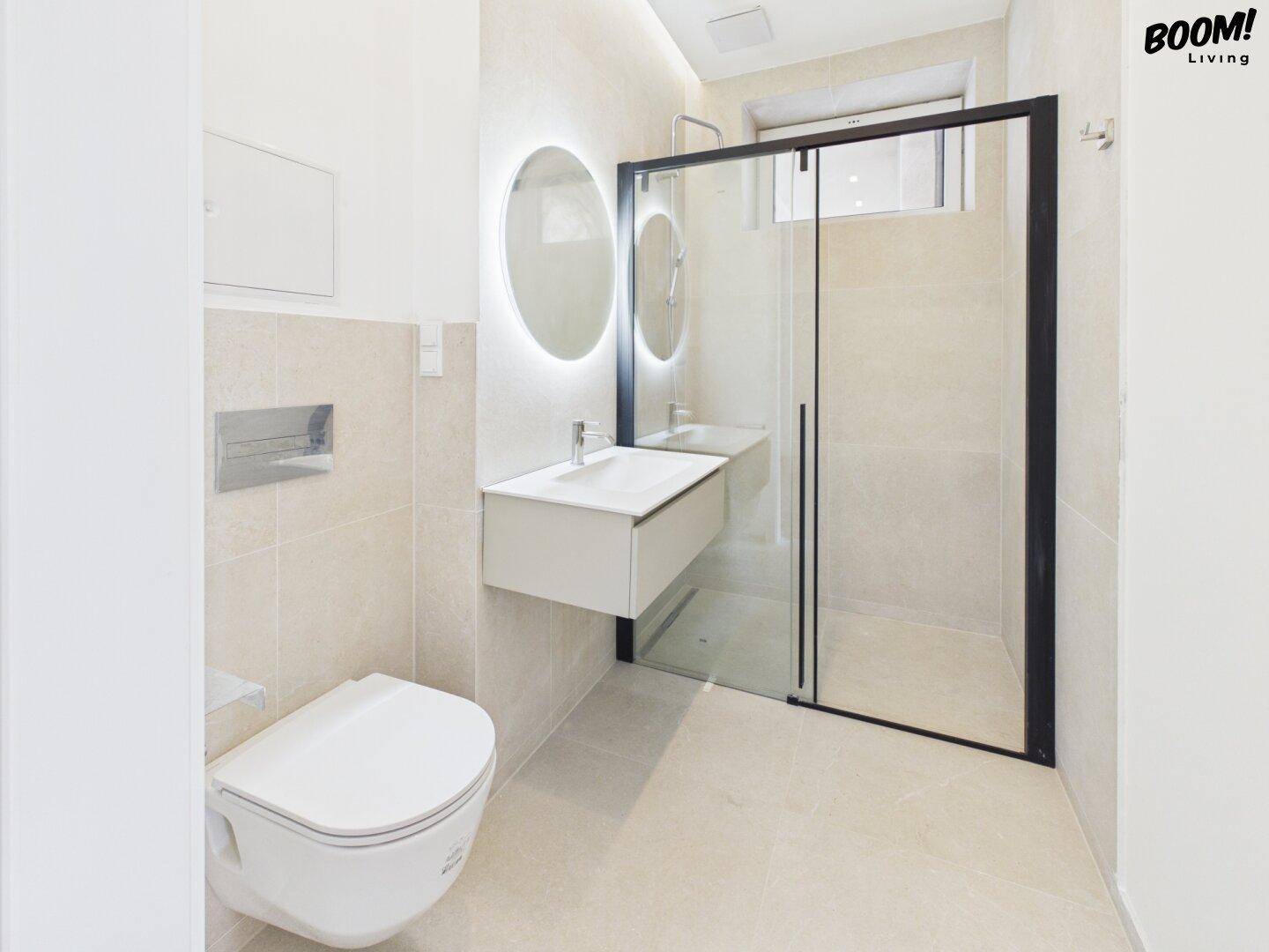 Modernes Badezimmer mit beigen Fliesen, schwebendem Waschtisch und einer geräumigen begehbaren Dusche.