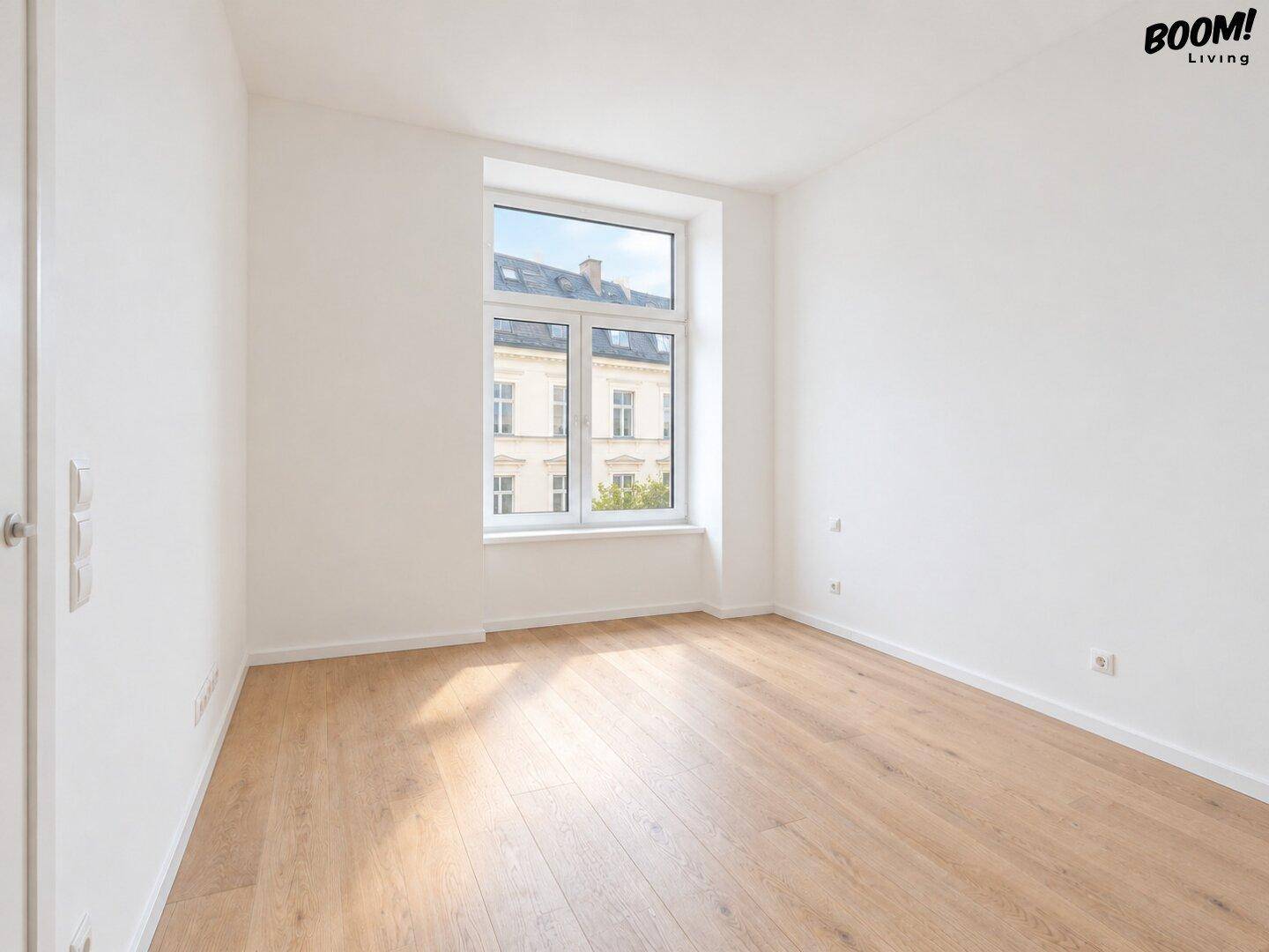 Helles, leeres Zimmer mit Holzboden und einem großen Fenster, ideal als Schlaf- oder Arbeitszimmer.