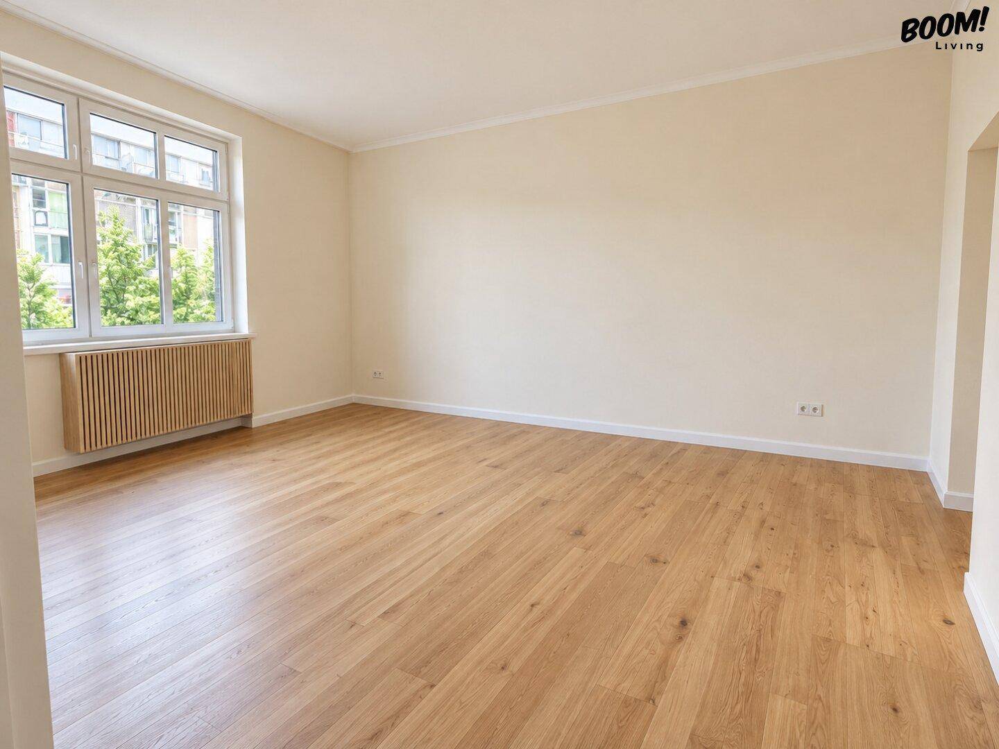 Leerer Raum mit hellem Holzboden und großem Fenster, bereit zur individuellen Gestaltung.