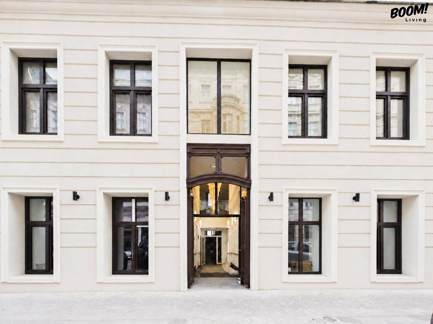 Elegante Fassade eines klassischen Gebäudes mit großen Fenstern und einem einladenden Eingangsbereich, der in einen Innenhof führt.