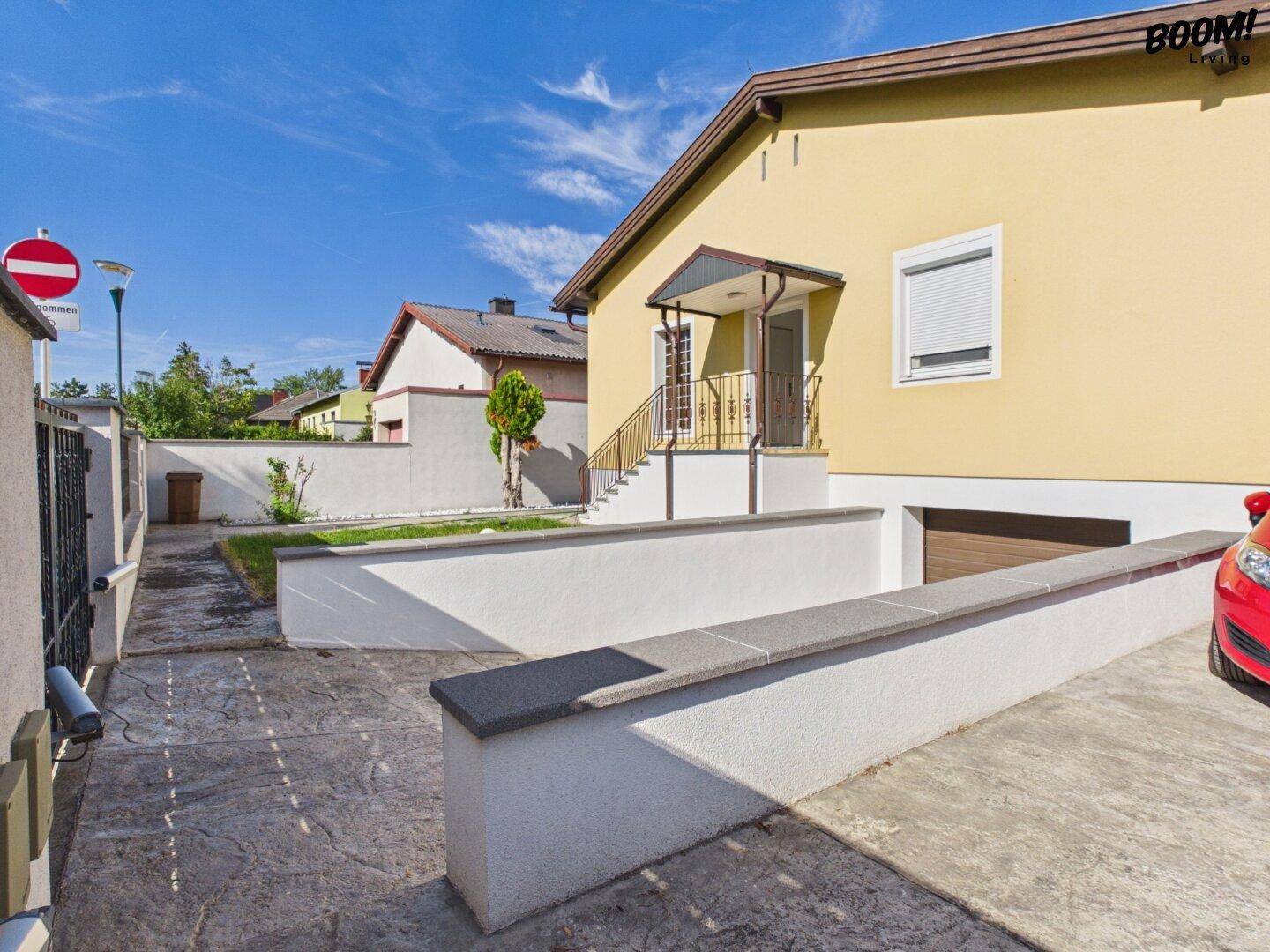 Einfahrt zum Haus mit Garagenzugang und seitlichem Weg unter strahlend blauem Himmel.