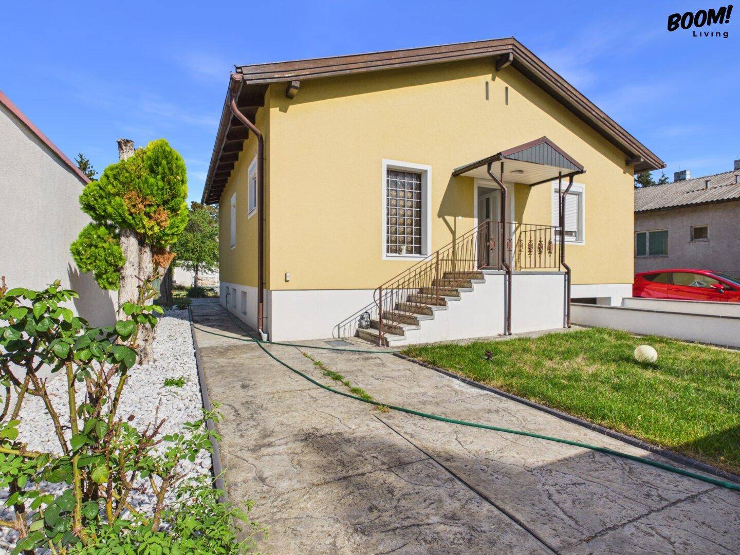 Seitenansicht des gelben Hauses mit Eingangsbereich, Treppe und gepflasterter Zufahrt.