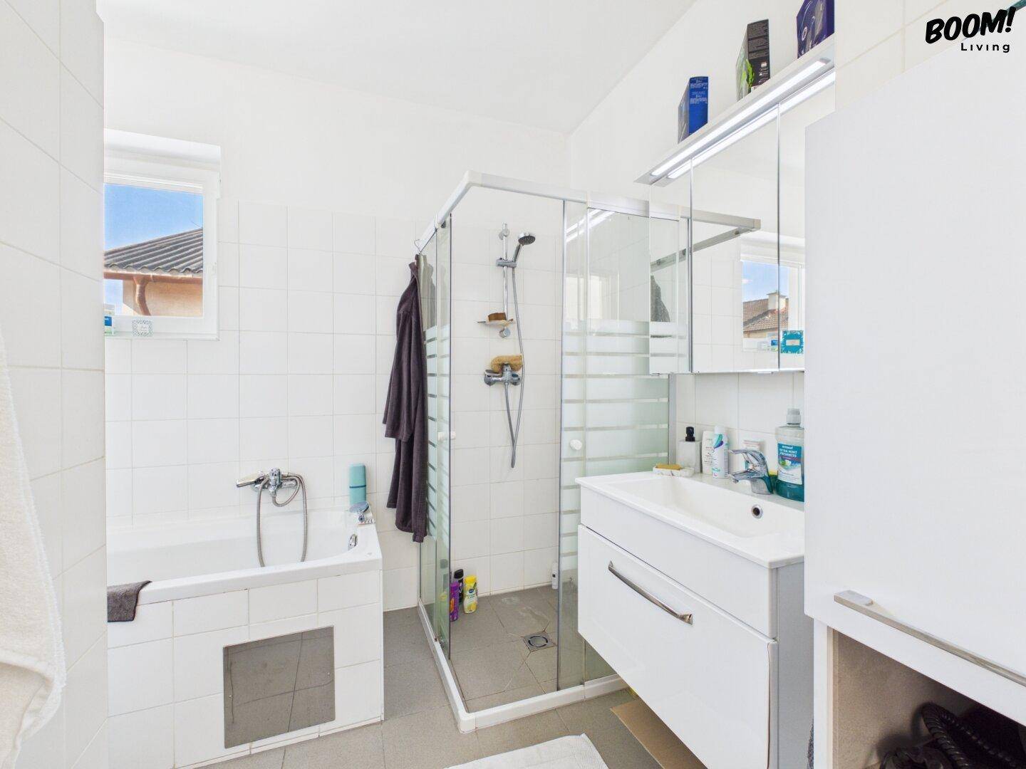 Helles Badezimmer mit Badewanne, Duschkabine und Fenster.