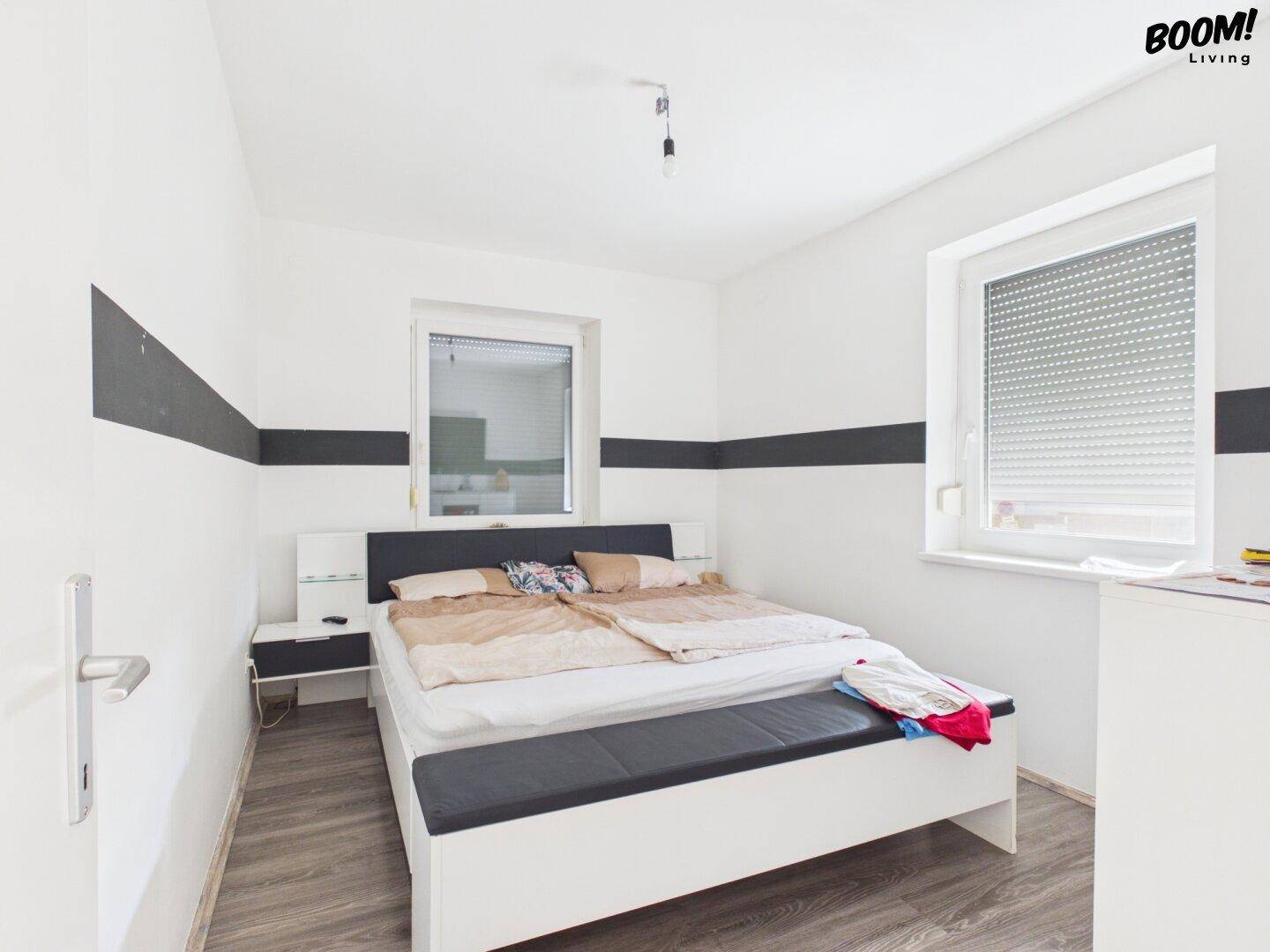 Schlafzimmer mit Doppelbett, modernem Bodenbelag und Fenster mit Rollladen.