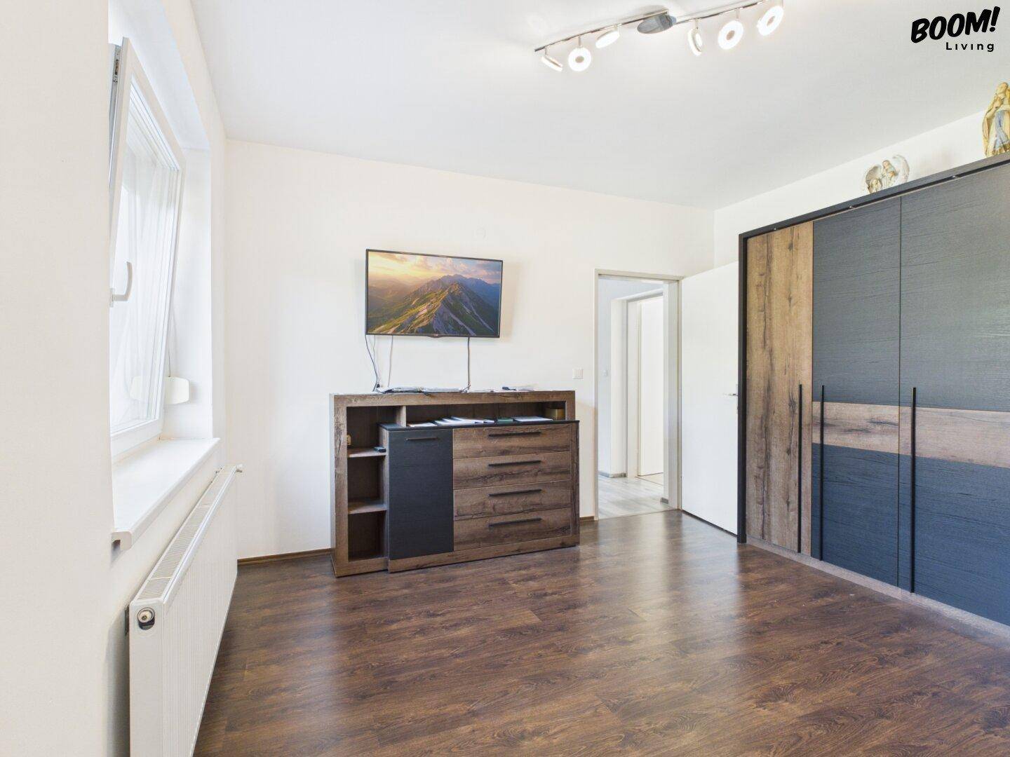 Geräumiges Schlafzimmer mit dunklem Boden, großem Kleiderschrank und Fernseher.