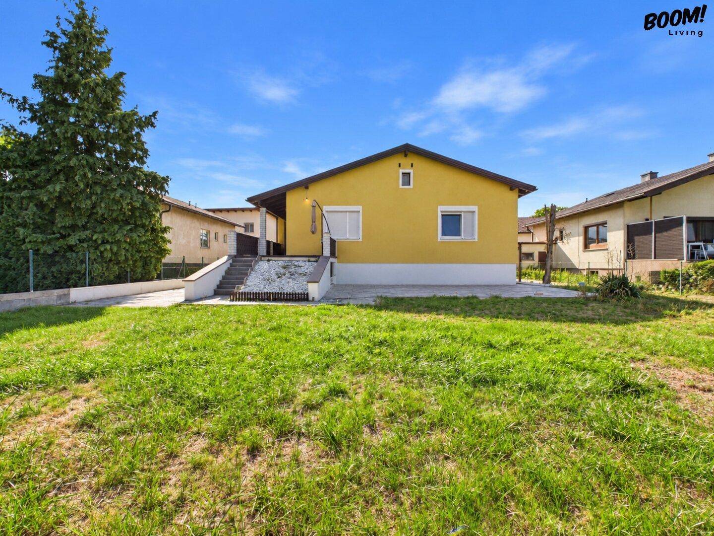 Rückansicht des gelben Einfamilienhauses mit großem Rasenbereich und blauer Himmel.