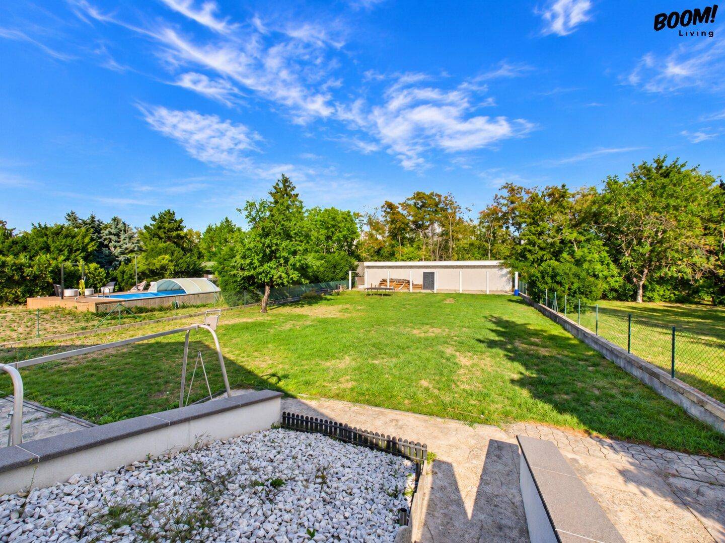 Weitläufiger Gartenbereich mit Rasenfläche, Bäumen und einem Pool im Hintergrund.