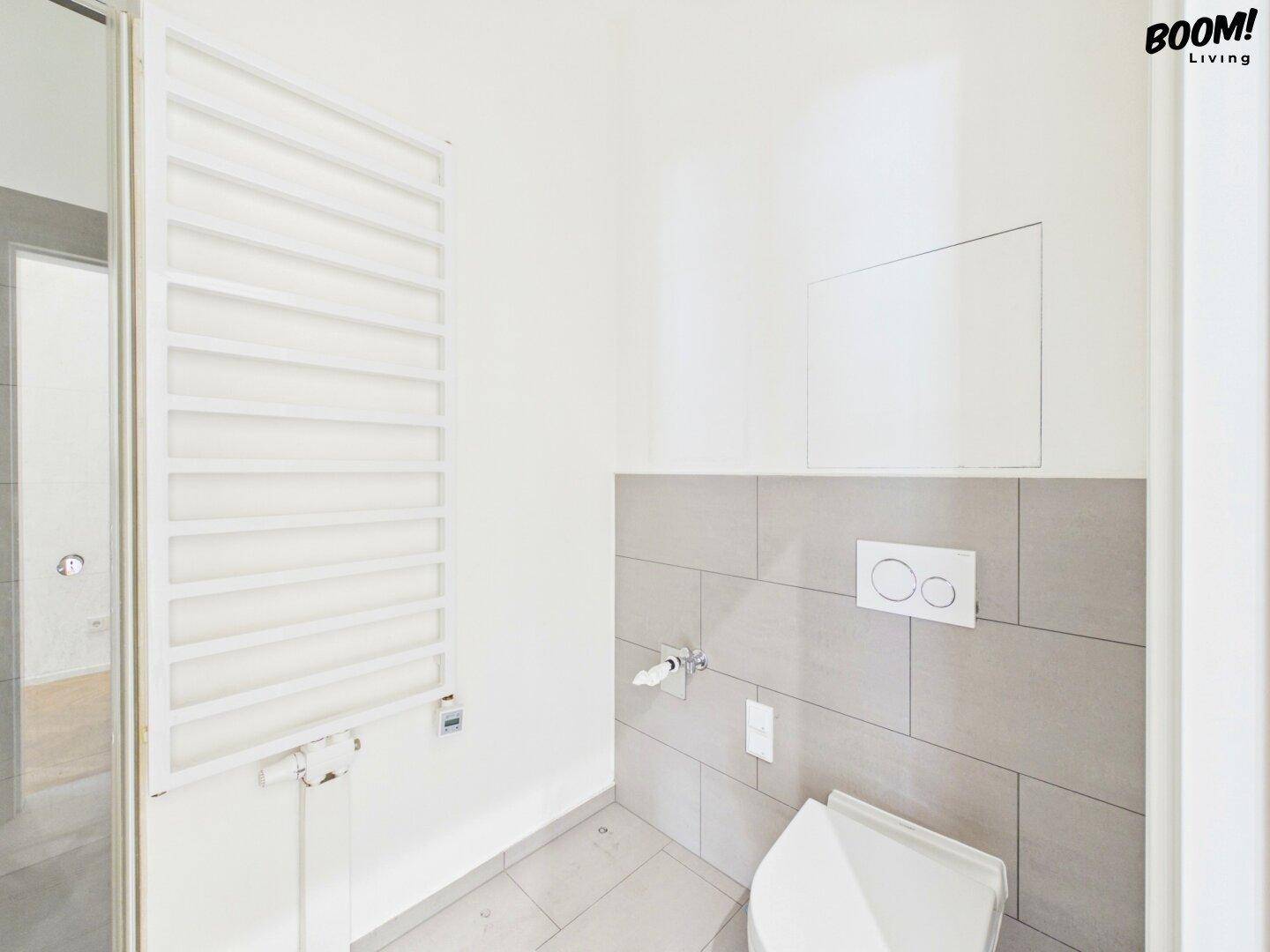 Modernes Gäste-WC mit Wand-WC, grauen Fliesen und beheiztem Handtuchhalter.