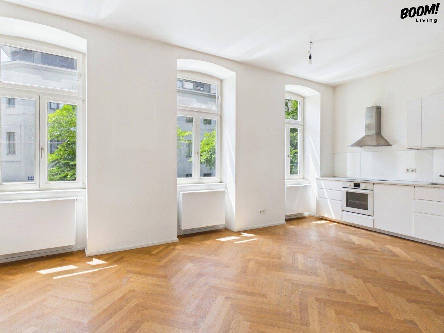 Lichtdurchfluteter, leerer Wohn-Essbereich mit Küchenzeile und elegantem Fischgrätparkett.