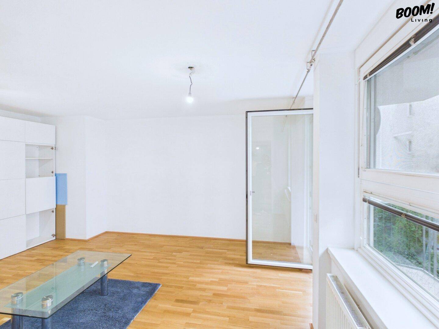 Helles, leeres Wohnzimmer mit Parkettboden und großen Fenstern zum Außenbereich.