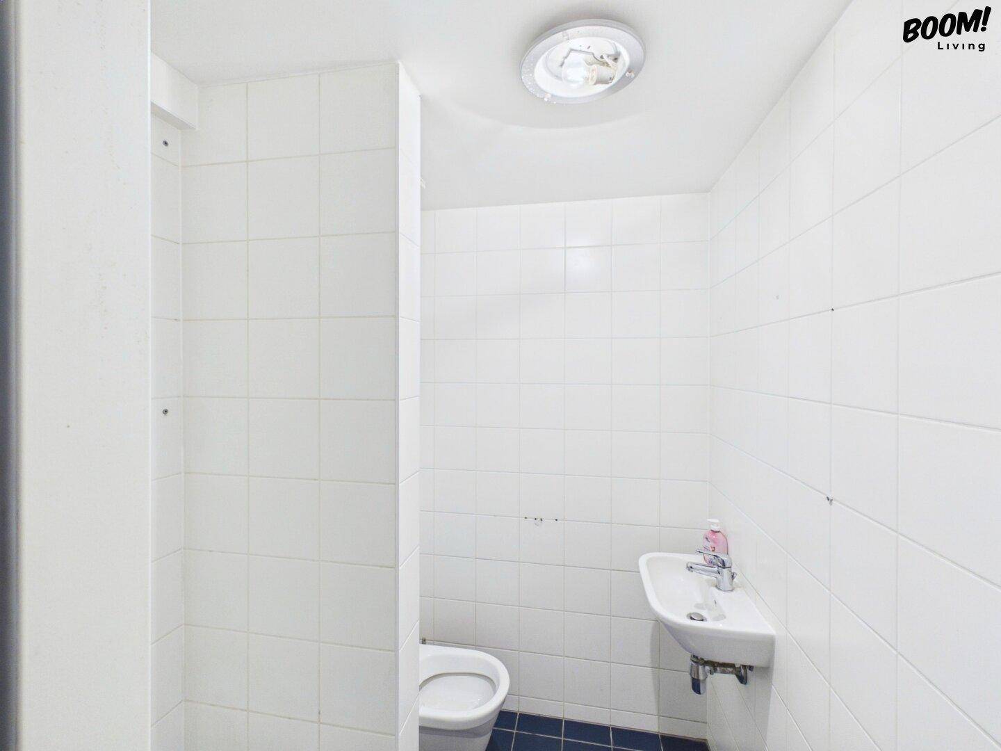 Einfaches Gäste-WC mit weißen Fliesen und grundlegender Sanitärausstattung.