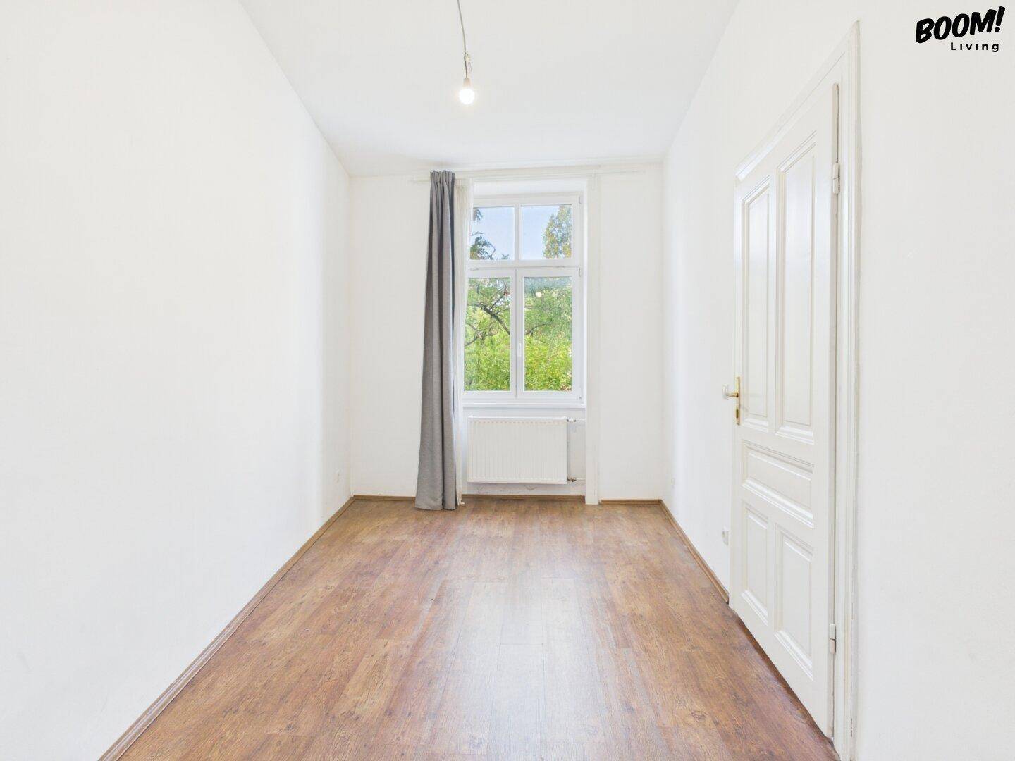 Leeres Schlafzimmer mit Holzboden und einem großen Fenster, das viel Tageslicht hereinlässt.