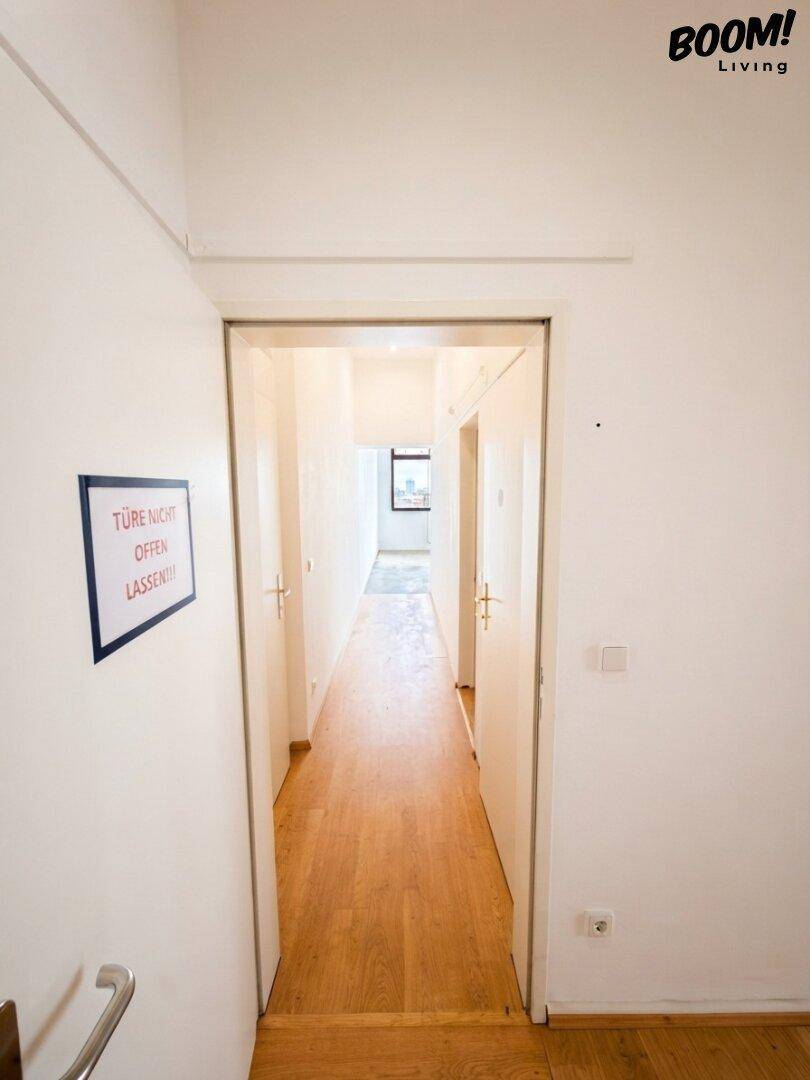 Langer Flur mit Holzparkettboden und weißen Wänden, der zu weiteren Räumen führt.