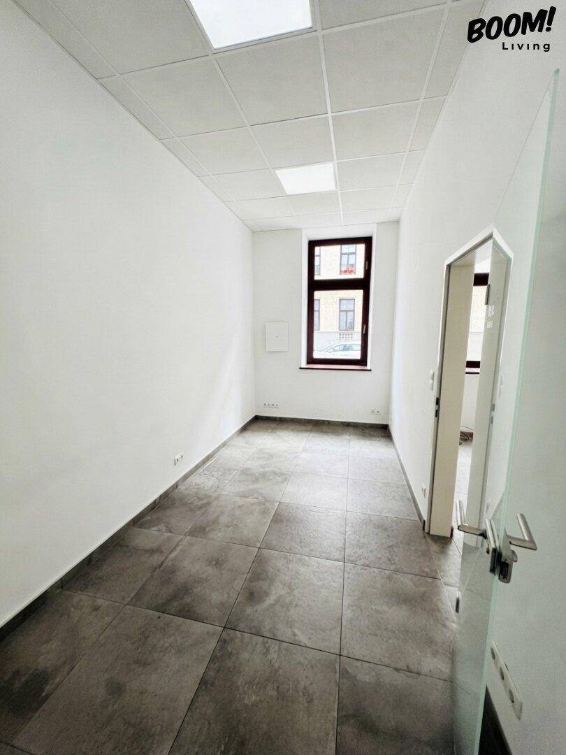 Heller Büroraum mit grauen Fliesen, weißen Wänden und einem Fenster mit Blick nach draußen.