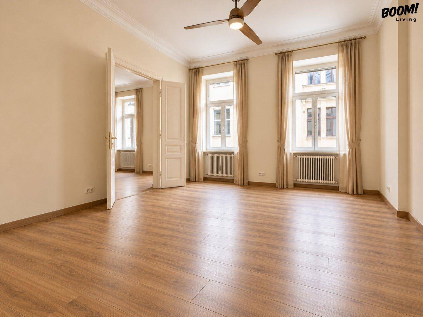 Geräumiges Wohnzimmer mit Holzboden und hohen Fenstern, das den Blick in einen weiteren Raum freigibt.
