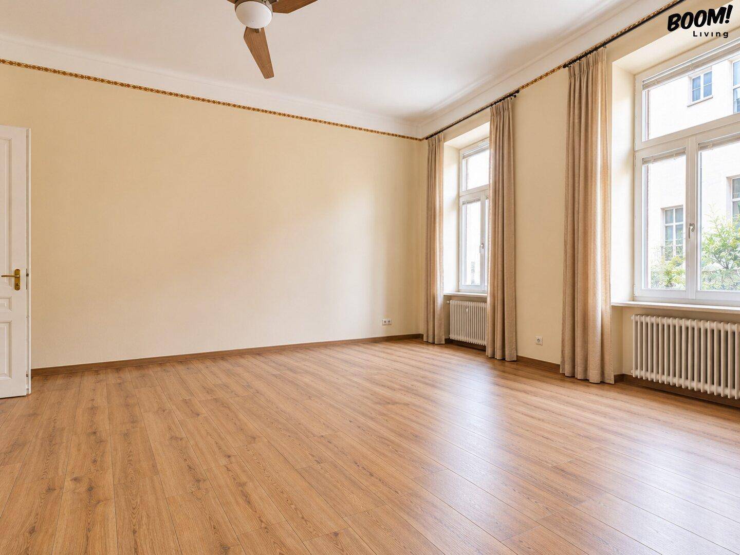 Großes, helles Zimmer mit Holzboden, hohen Fenstern und Deckenventilator, ideal für Wohnzwecke.