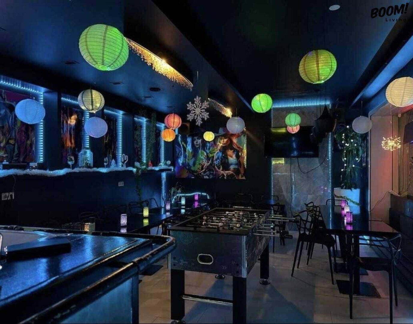 Ein dunkler Lounge-Bereich mit bunten Papierlaternen, einem Tischfußballspiel und Neonbeleuchtung.
