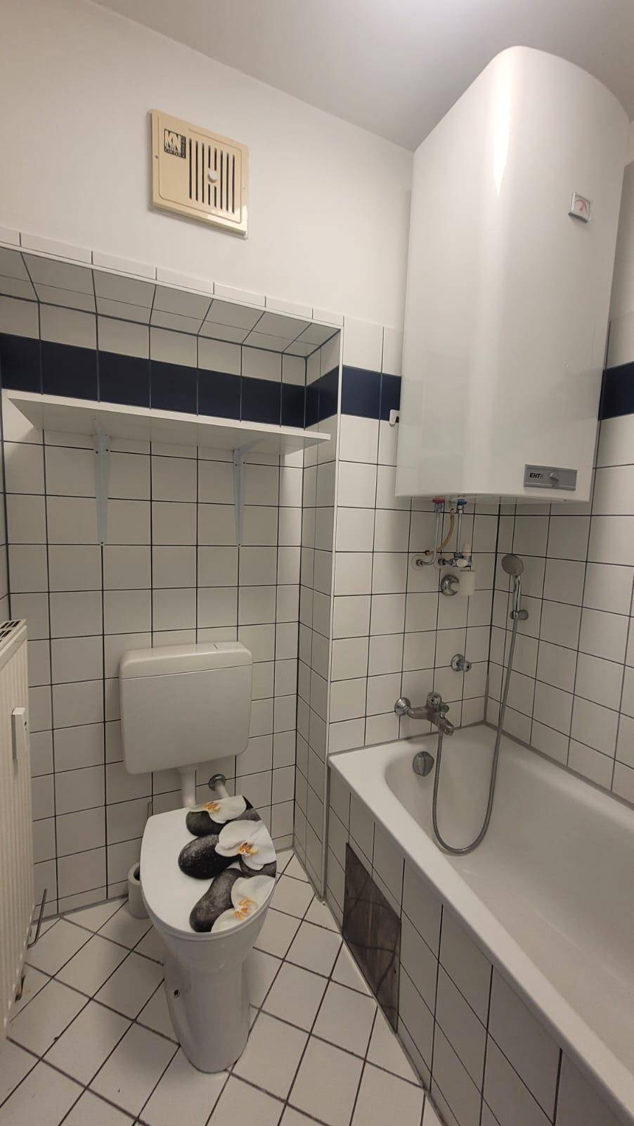Funktionales Badezimmer mit Badewanne, Toilette und Wandheizkörper, ausgestattet mit weißen Fliesen.