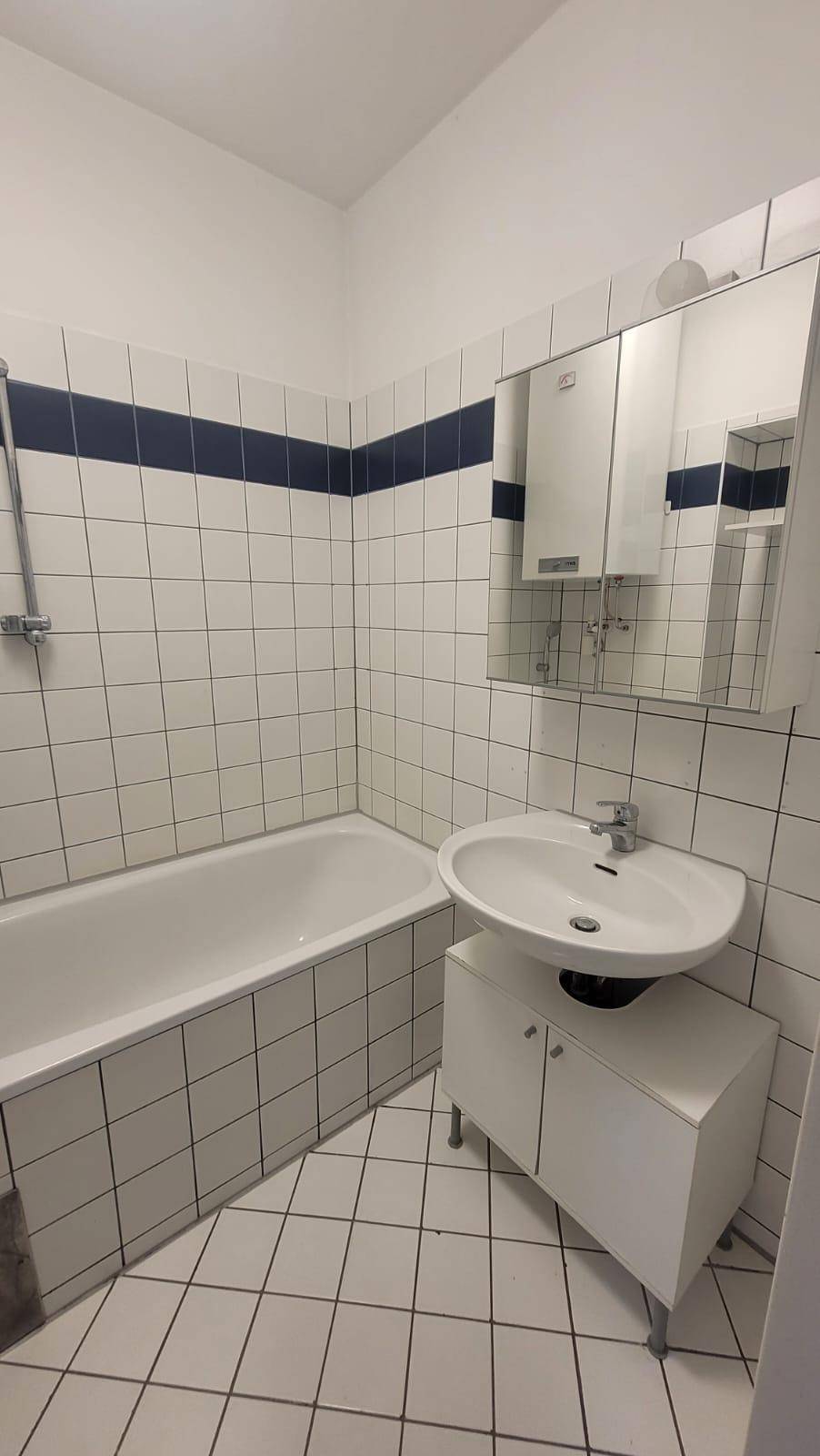 Helles Badezimmer mit Badewanne, Waschbecken und weißen Fliesen mit blauer Akzentlinie.