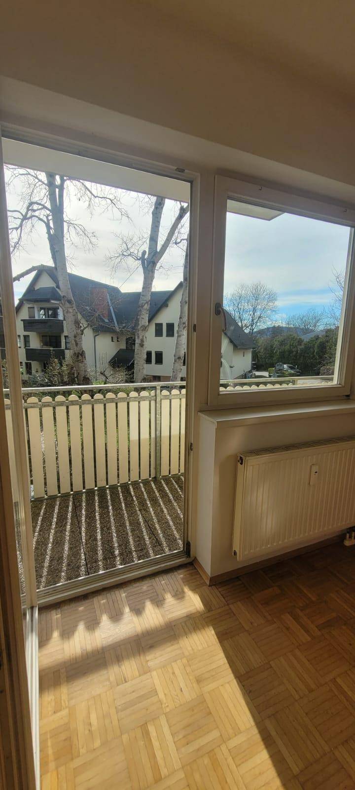 Helles Wohnzimmer mit Blick auf den Balkon und die umliegenden Gebäude, bietet viel Tageslicht.