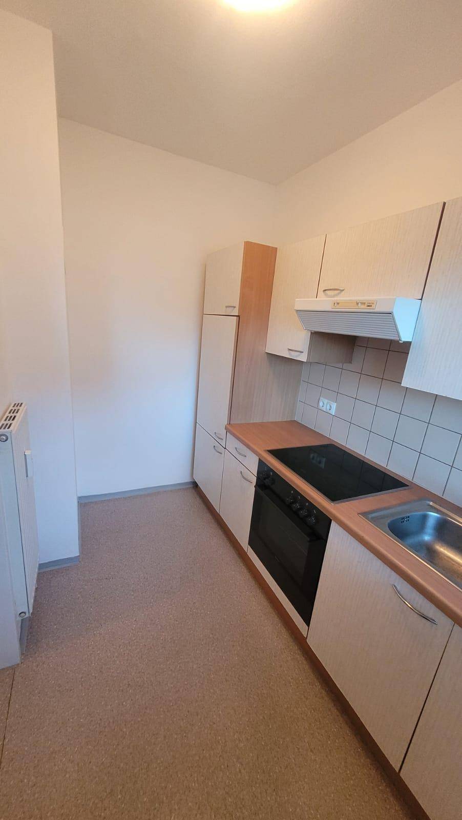 Einfache Küche mit Einbauschränken, Kochfeld und Heizkörper, bietet grundlegende Ausstattung.