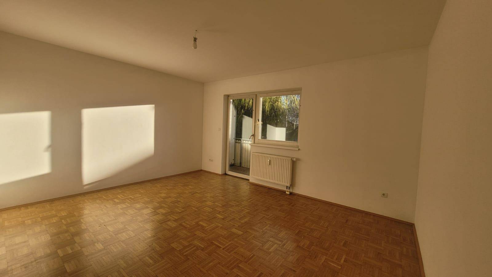 Geräumiges Wohnzimmer mit Parkettboden und Zugang zum Balkon, lichtdurchflutet und einladend.