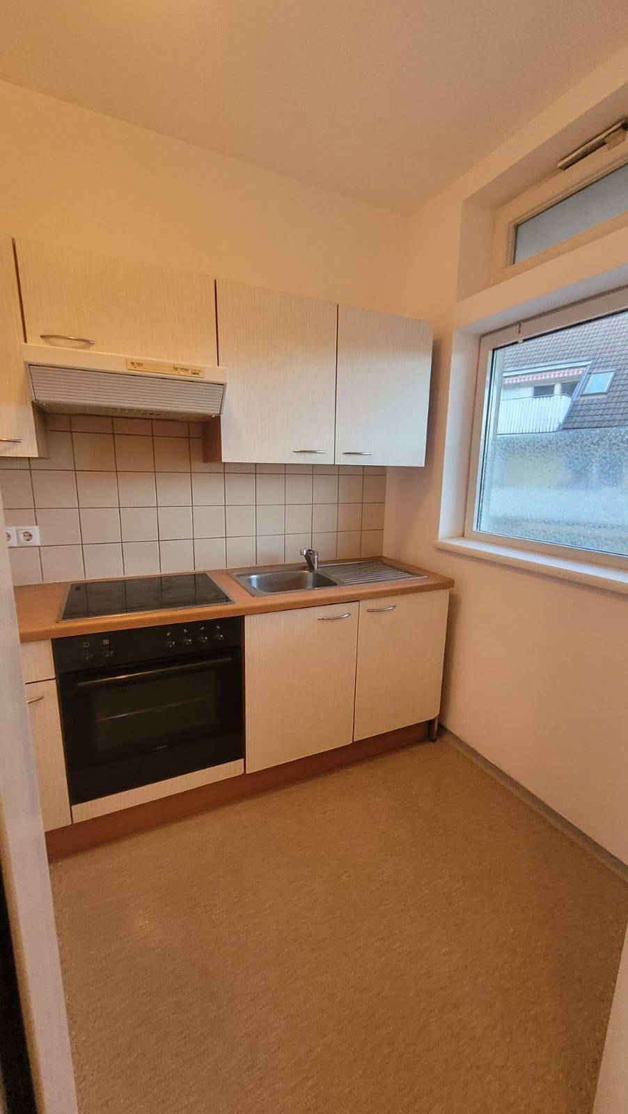 Helle Küche mit Fenster, Einbauschränken und Spüle, bietet ausreichend Arbeitsfläche.