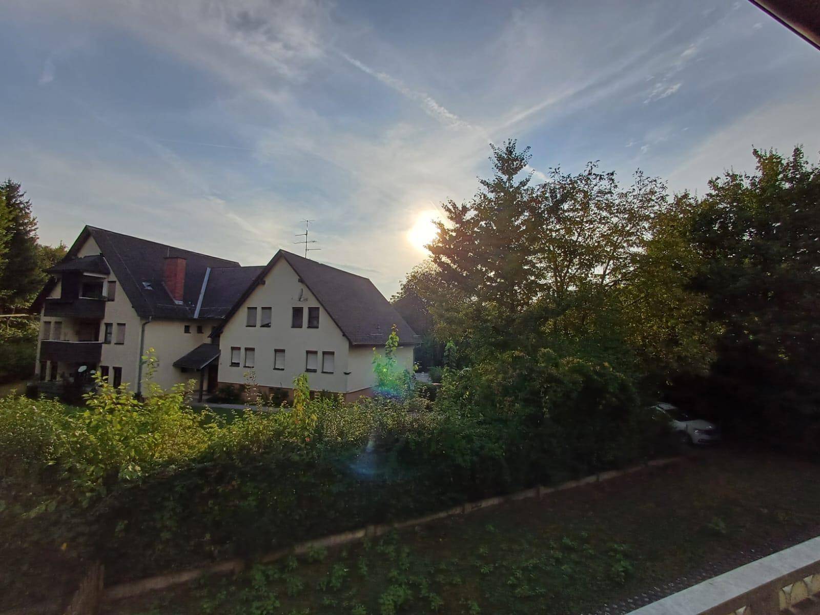 Ansicht des Gebäudes bei Sonnenuntergang, umgeben von üppigem Grün und Bäumen.