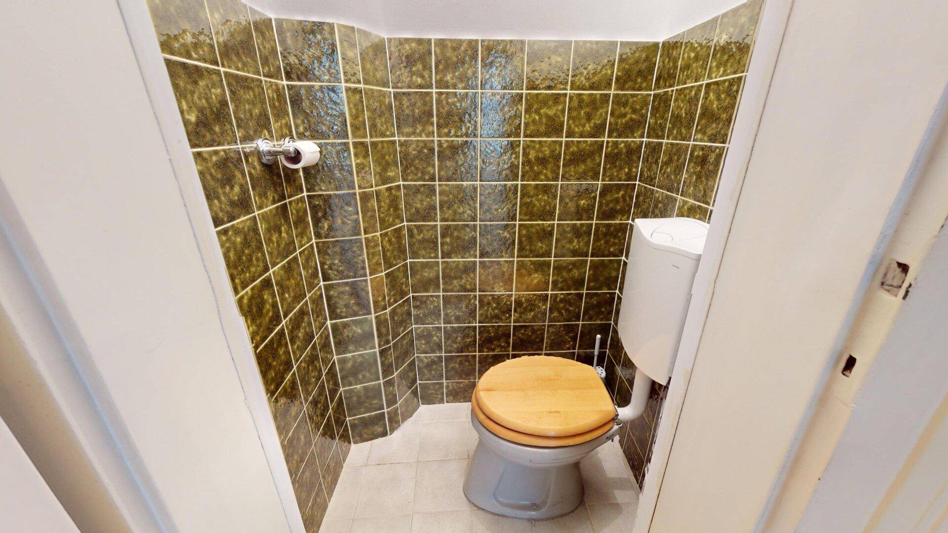 Separate Toilette mit dunkelgrünen Fliesen und einem WC mit Holzdeckel.