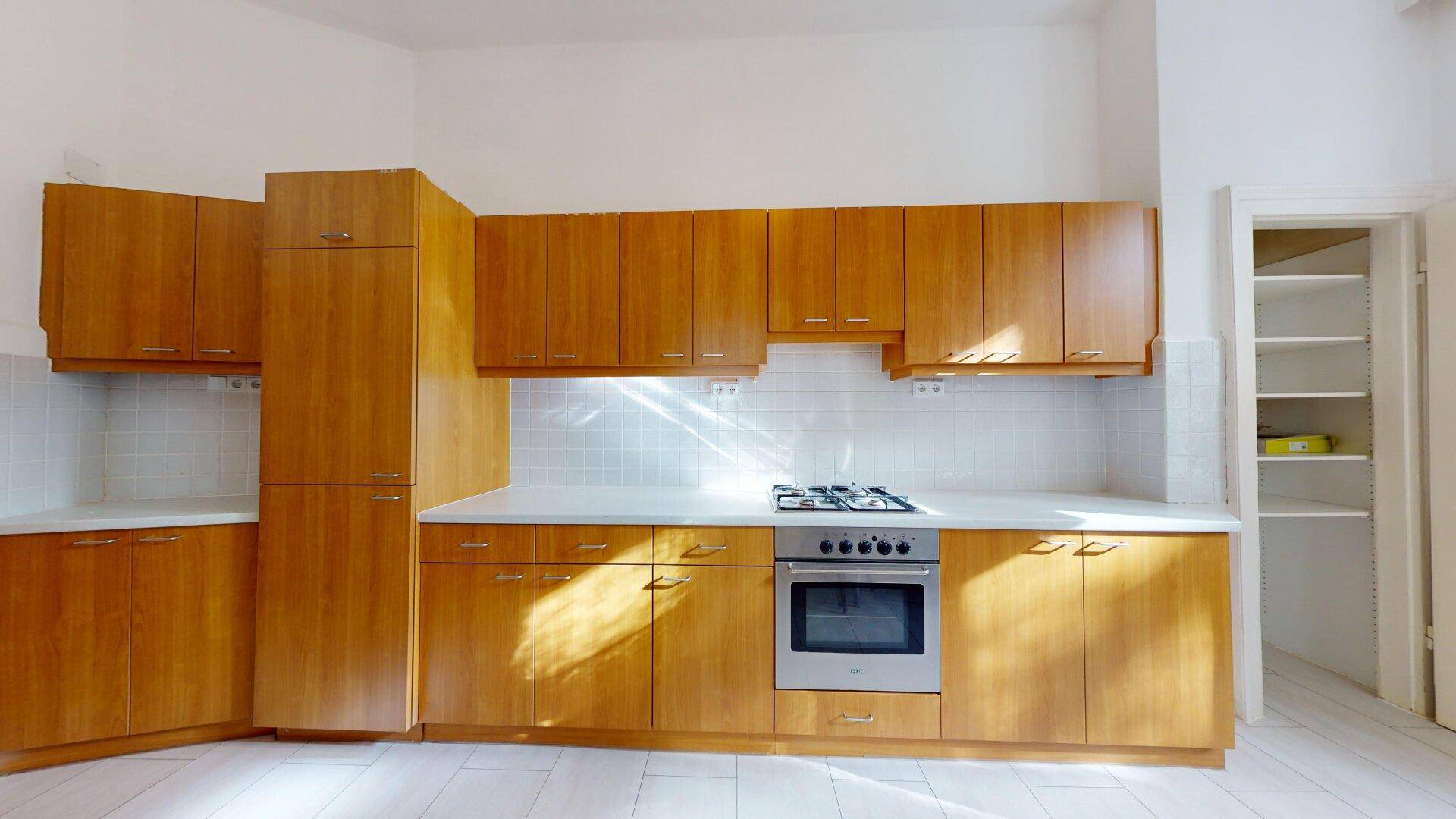 Funktionale Küche mit Holzschränken, Gasherd und integriertem Backofen sowie einer Speisekammer.
