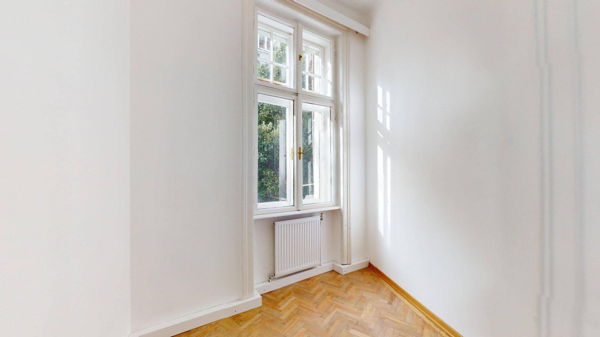 Kleineres Zimmer mit Fischgrätparkett und einem großen Fenster, ideal als Schlaf- oder Arbeitszimmer.