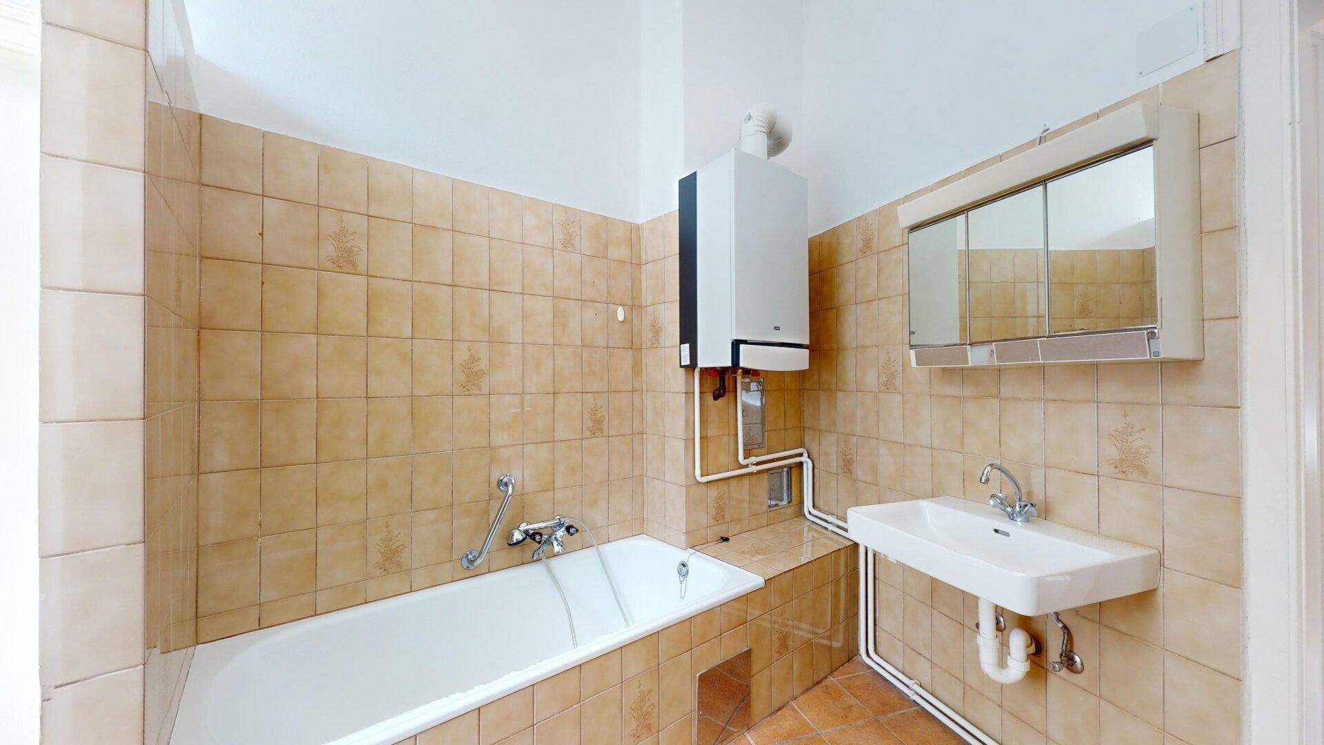 Gefliestes Badezimmer mit Badewanne, Waschbecken und Spiegelschrank, in einem älteren Stil.