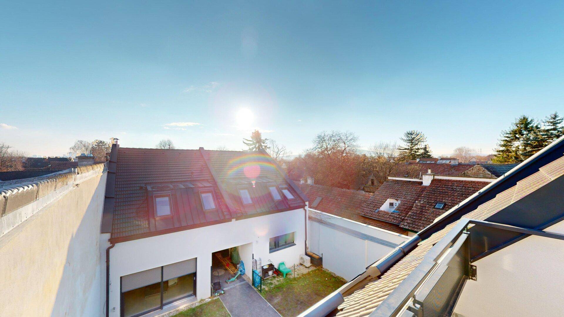 Dachlandschaft des Gebäudes mit Blick auf die umliegende Bebauung und einen Dachterrassenbereich bei Sonnenschein.