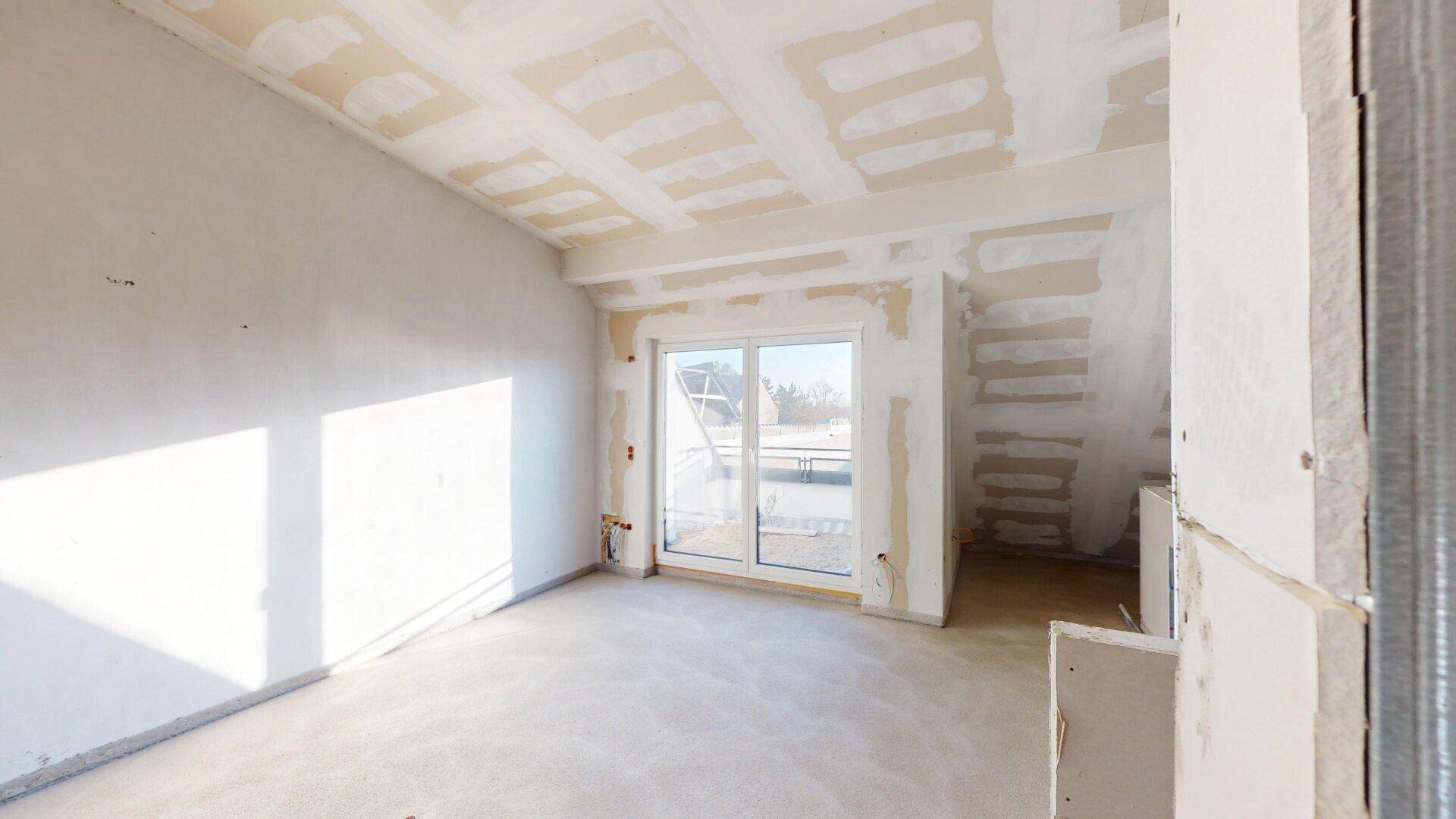 Unfertiger Innenraum im Dachgeschoss mit Zugang zu einem Balkon oder einer Terrasse.