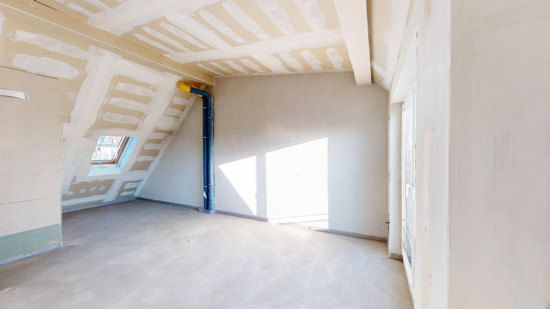 Unfertiger Raum im Dachgeschoss mit schräger Decke und einem Dachfenster für natürliches Licht.
