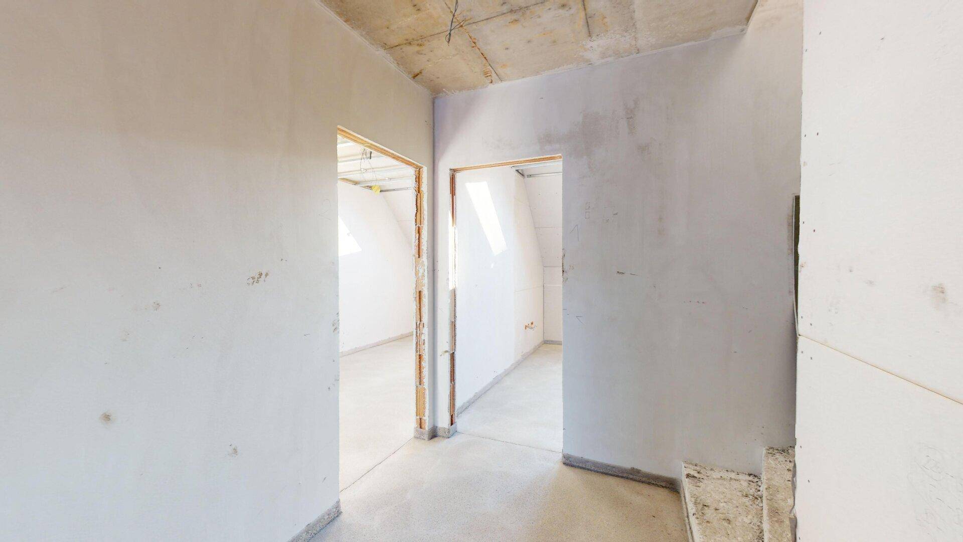Unfertiger Flurbereich im Dachgeschoss mit schrägen Wänden und Betonboden.