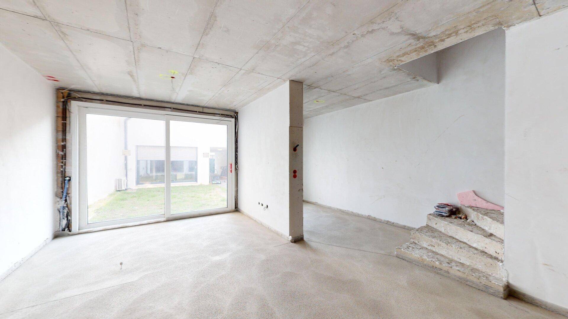 Heller Rohbau-Raum im Erdgeschoss mit Schiebetür und sichtbaren Treppenstufen.