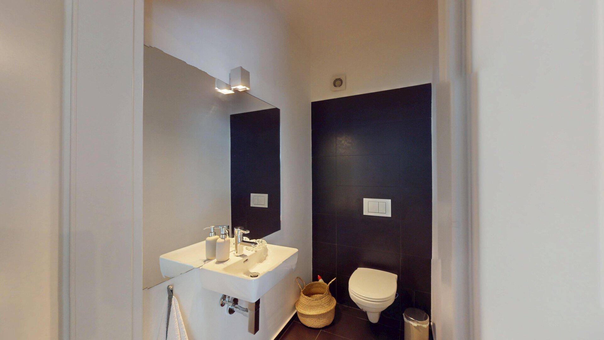 Modernes Gäste-WC mit wandhängender Toilette, stilvollem Waschbecken und dunklen Akzentfliesen.