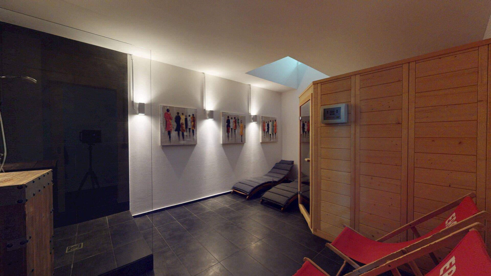 Entspannender Wellnessbereich mit Sauna, Liegestühlen und einer modernen Duschzone.