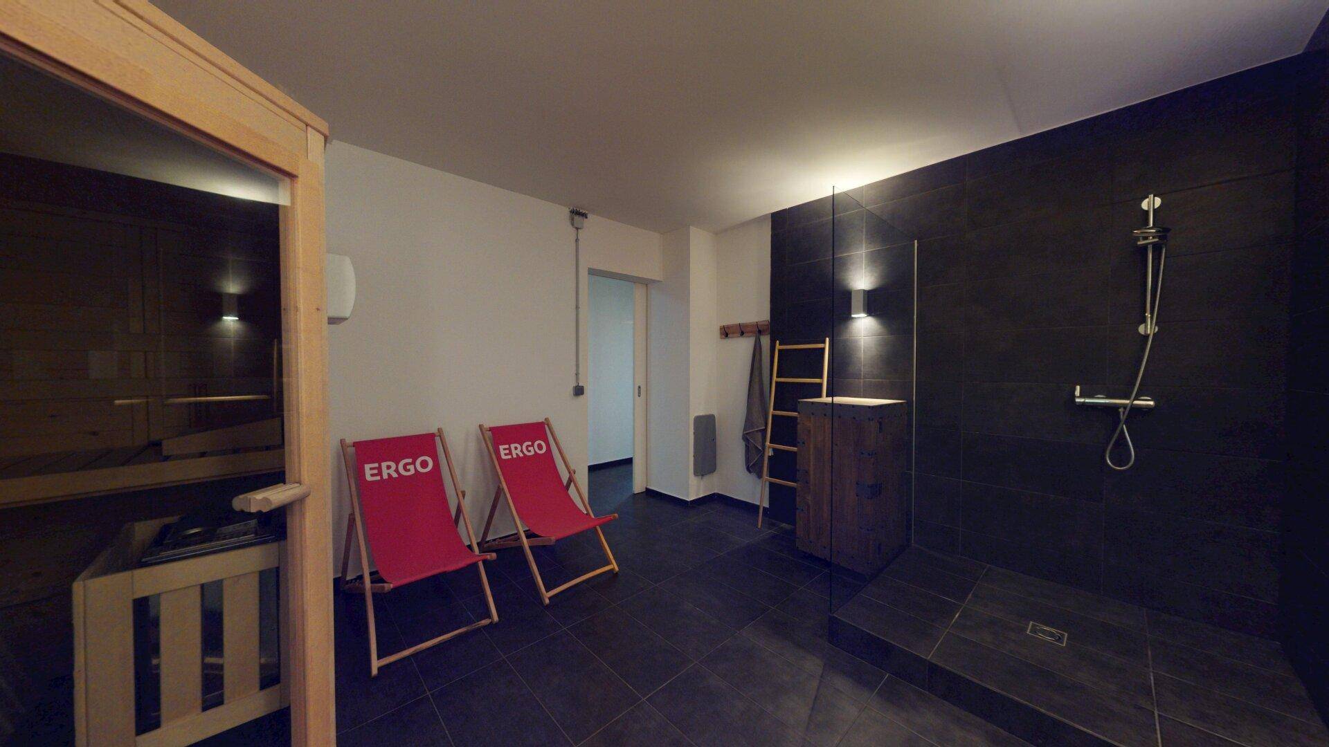 Gemütlicher Wellnessbereich mit Holzsauna, großer Dusche und bequemen Liegestühlen.
