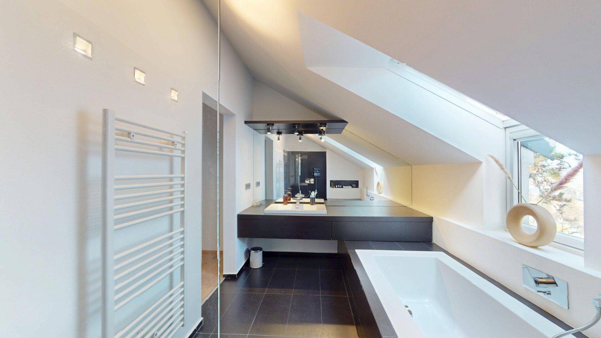 Stilvolles Dachgeschossbad mit modernem Waschtisch, Badewanne und viel Tageslicht durch das Dachfenster.