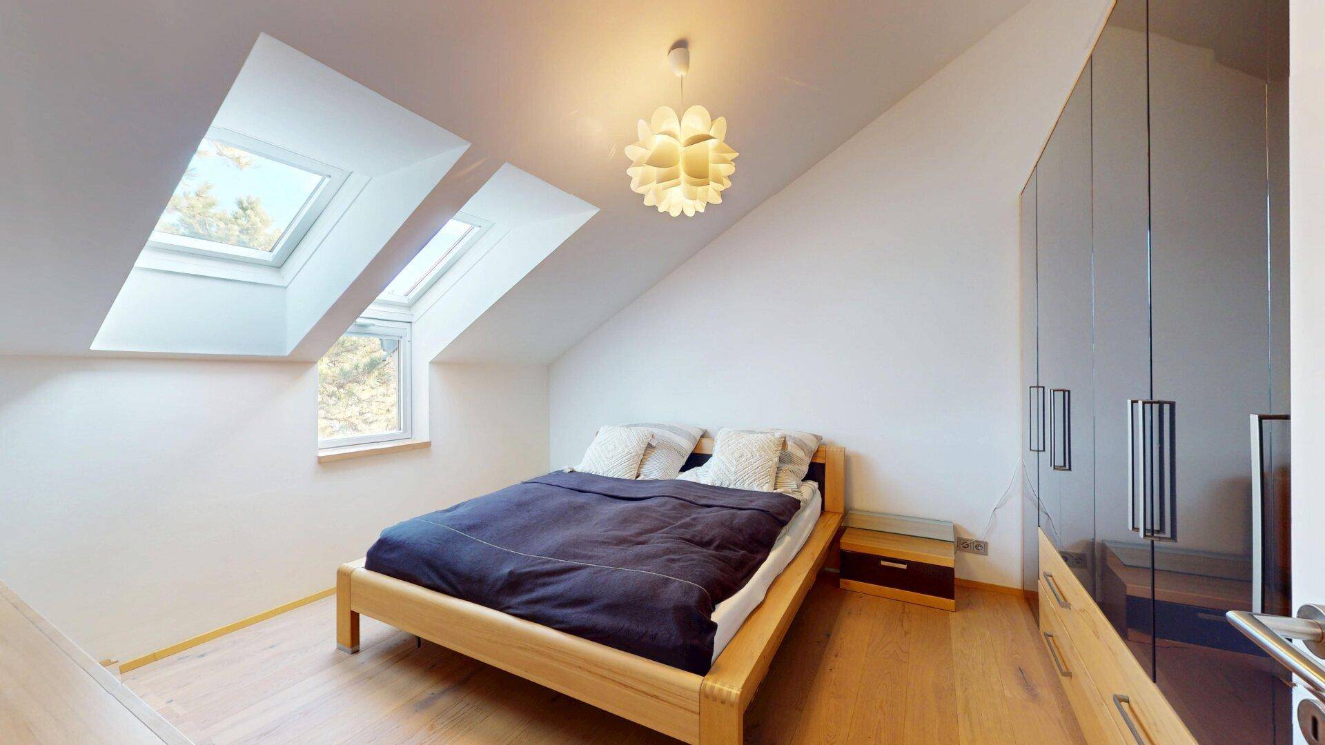 Gemütliches Schlafzimmer im Dachgeschoss mit Doppelbett, Kleiderschrank und hellen Dachfenstern.