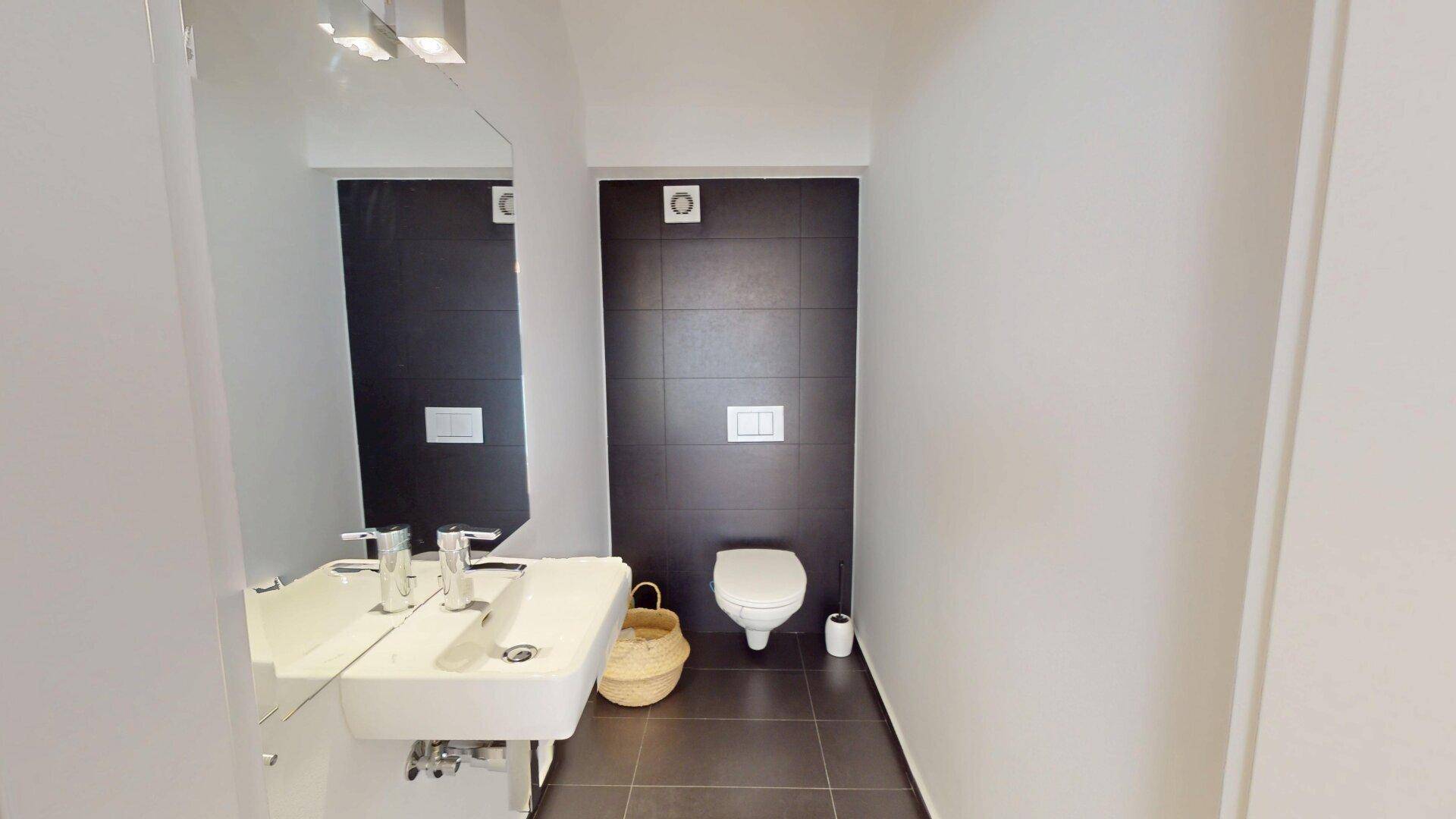 Modernes Gäste-WC mit wandhängender Toilette, stilvollem Waschbecken und dunklen Akzentfliesen.