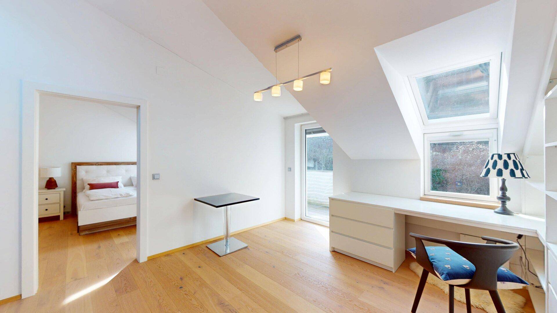 Geräumiges Arbeitszimmer im Dachgeschoss mit Schreibtisch, Regal und Zugang zum Balkon.