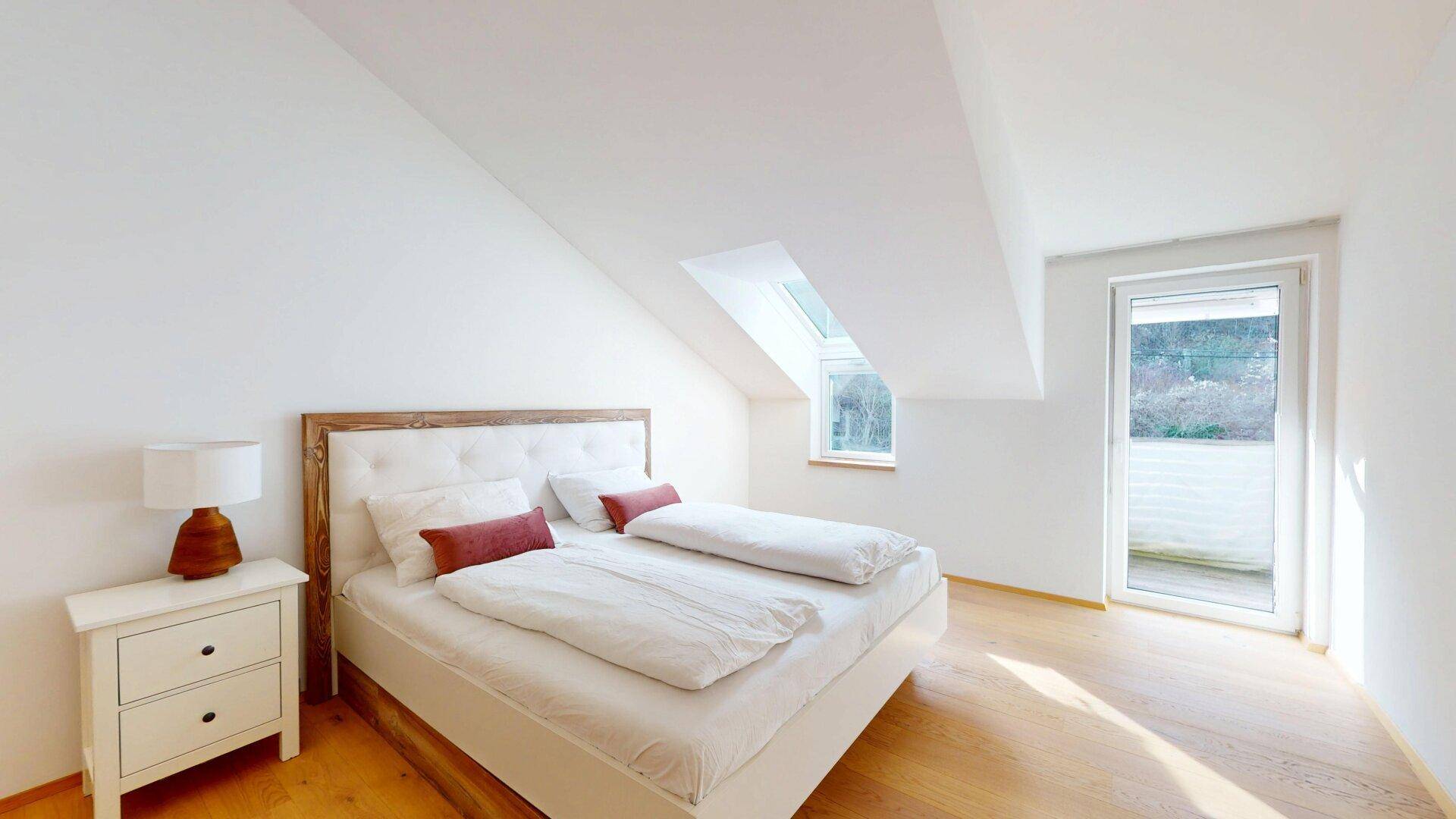 Helles Schlafzimmer im Dachgeschoss mit Doppelbett und direktem Zugang zu einem Balkon.