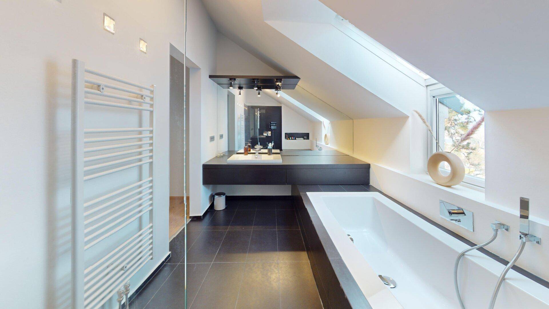 Modernes Badezimmer mit Badewanne, Einzelwaschbecken, beheiztem Handtuchhalter und Dachfenster.
