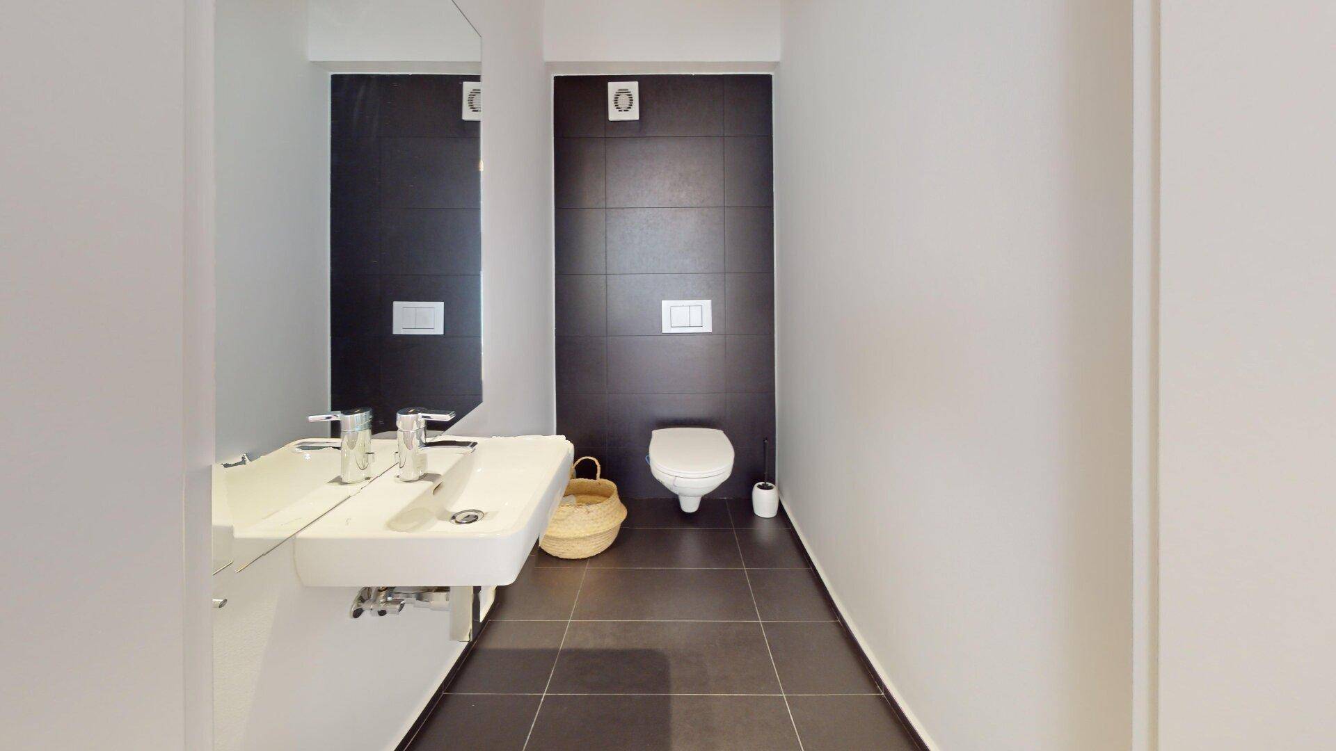 Kleines Gäste-WC mit modernem Waschbecken und dunklen Fliesen an der Wand.