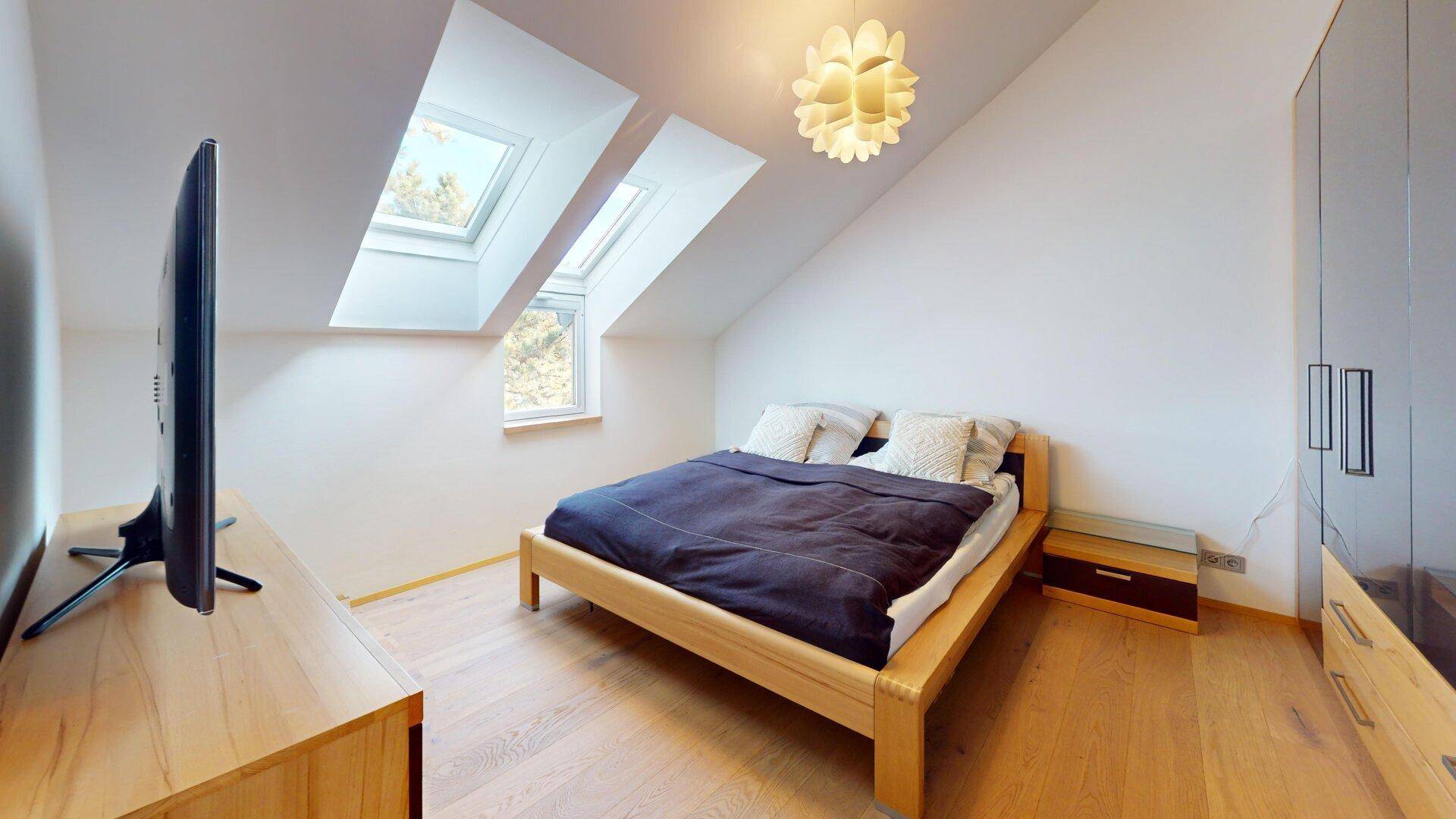 Gemütliches Schlafzimmer mit Holzboden, Dachschräge und zwei Dachfenstern für viel Licht.
